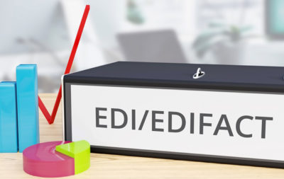 EDIFACT Software Ordner auf Schreibtisch mit EDI/EDIFACT Beschriftung neben Diagrammen